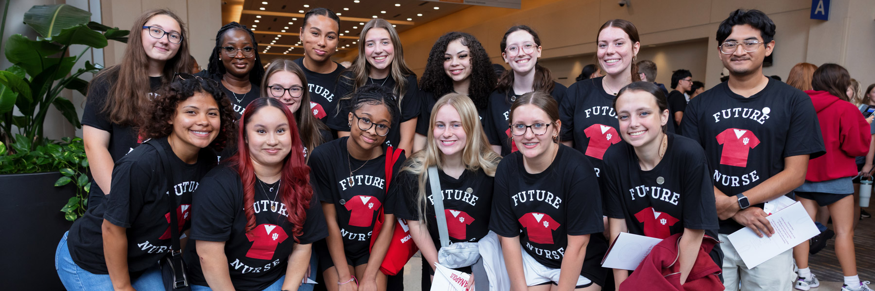 A diverse group of students wearing matching “Future Nurse” T-shirts pose together at an IU School of Nursing event, smiling while holding program materials.