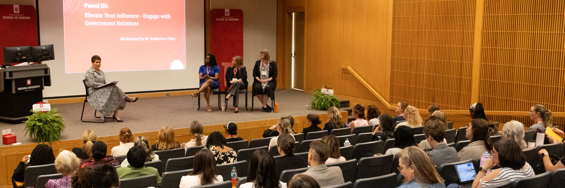 Panel discussion at an IU School of Nursing event titled “Elevate Your Influence – Engage with Government Relations,” with four speakers seated on stage before an audience.