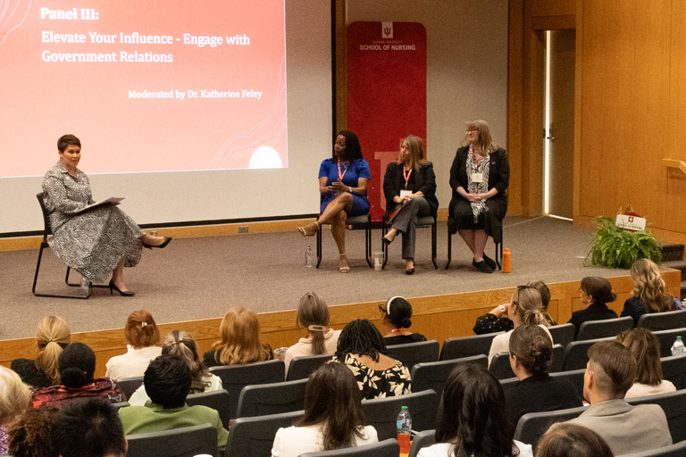 Panel discussion at an IU School of Nursing event titled “Elevate Your Influence – Engage with Government Relations,” with four speakers seated on stage before an audience.