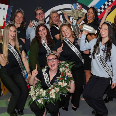Maxine Cosat, front center, and a group of eight other princesses wearing “500 Festival Princess 2026” sashes pose for a photo and celebrate together.