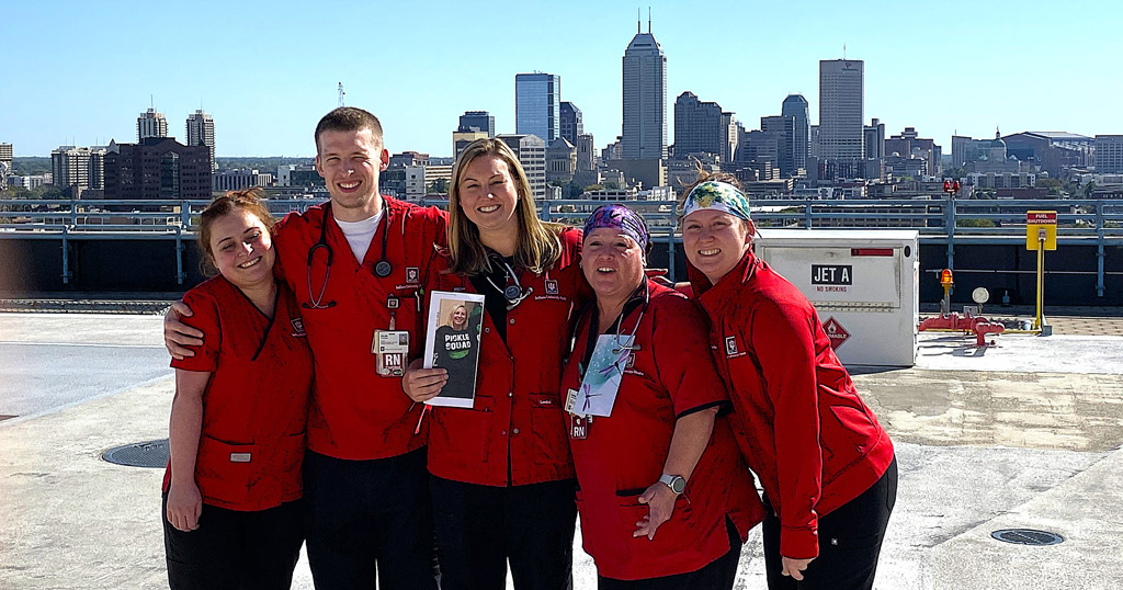 Five Indiana University Health employees stand on the rooftop with the Indianapolis skyline in the background