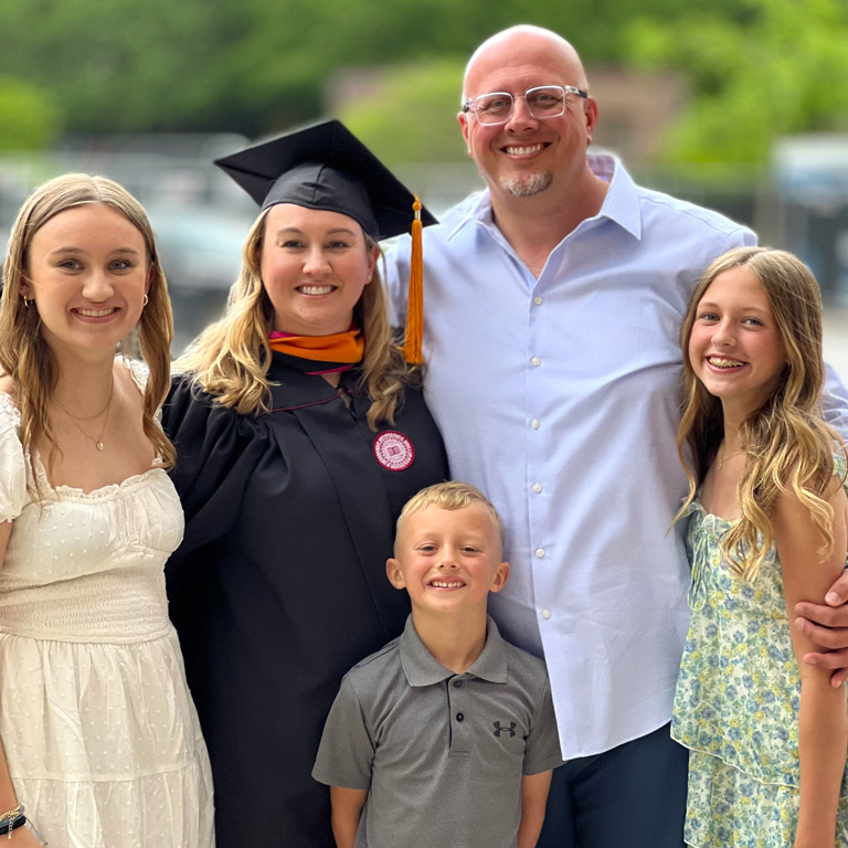 Krista Reed, in graduation regalia, poses for a photo with her family during the 2025 commencement season.