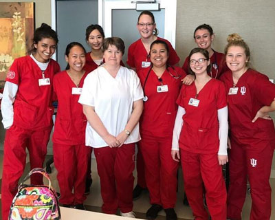 Marsha Hughes-Gay poses with IU School of Nursing students who are wearing their red scrubs.