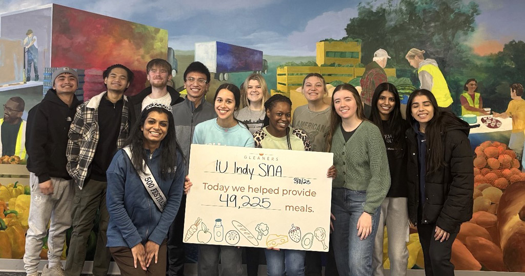 Group of IU Indy SNA students holding a sign that reads “Today we helped provide 49,225 meals,” standing in front of a food bank mural.