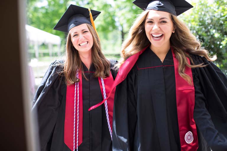 Two graduates in caps and gowns smiling broadly