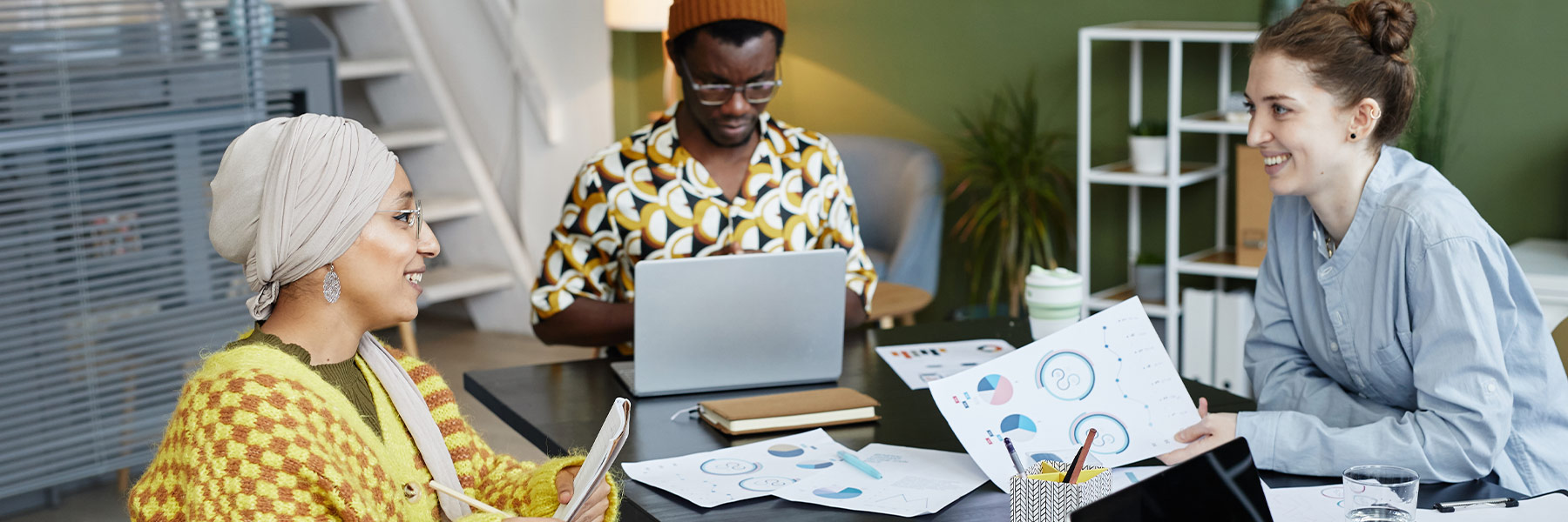 Three people working at a table filled with laptop and papers